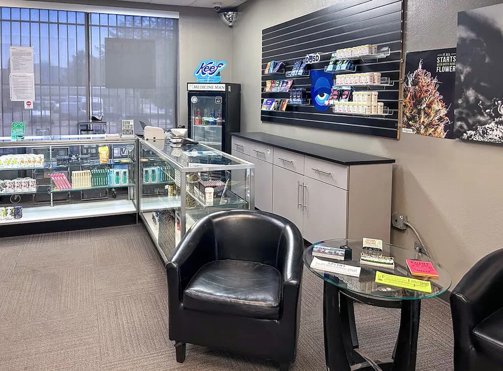 Interior of the Medicine Man Denver dispensary with glass display cases and a waiting area with black leather chairs.