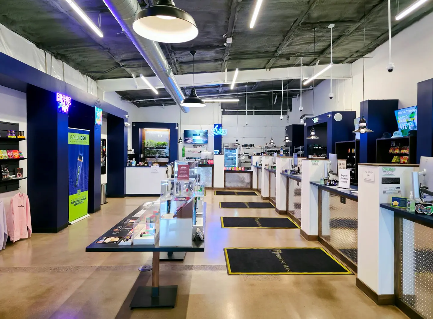 Contemporary interior of the Medicine Man Longmont dispensary with glass product tables, navy counters, and neon signage.